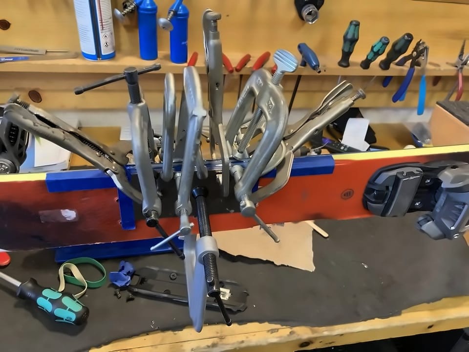 Row of clamps holding a top sheet repair on a ski