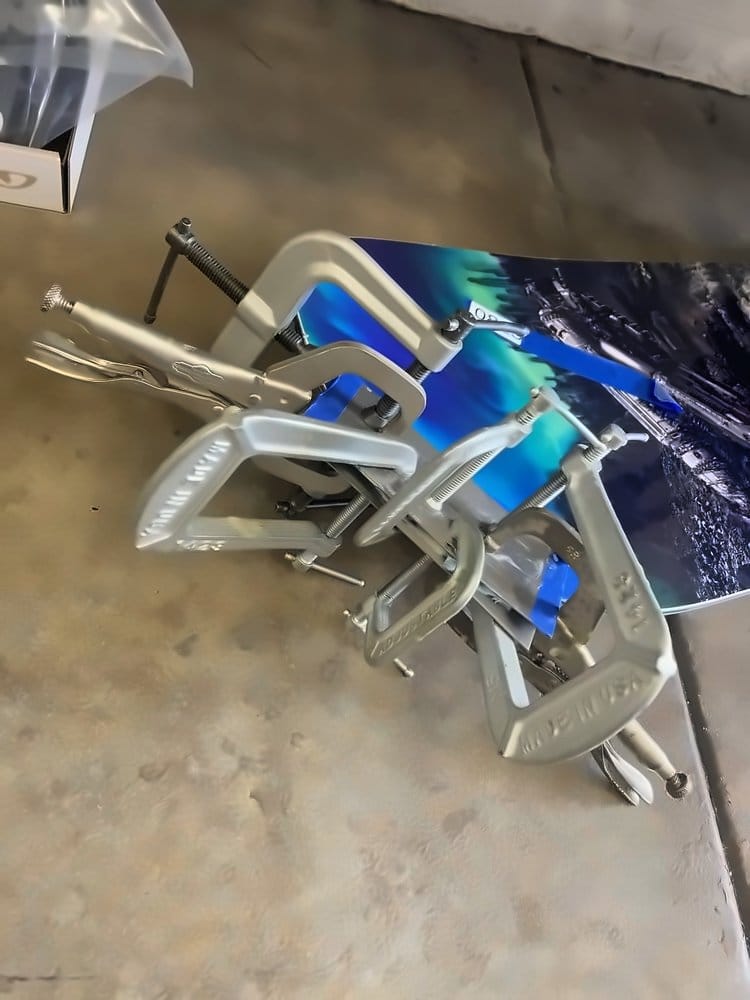 Clamps holding a snowboard repair with an aurora top sheet graphic