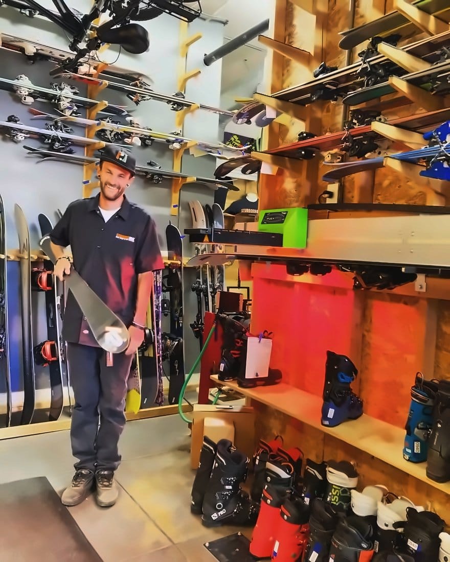 Smiling technician holding a K2 ski in front of the boot and ski wall