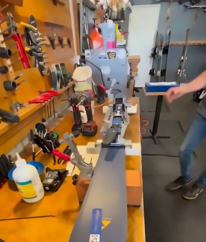 Ski clamped in a binding mounting jig, with the tool wall in the background