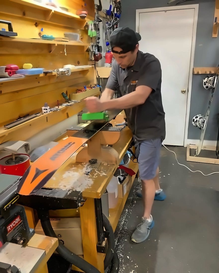 Technician planing an orange snowboard base at the bench