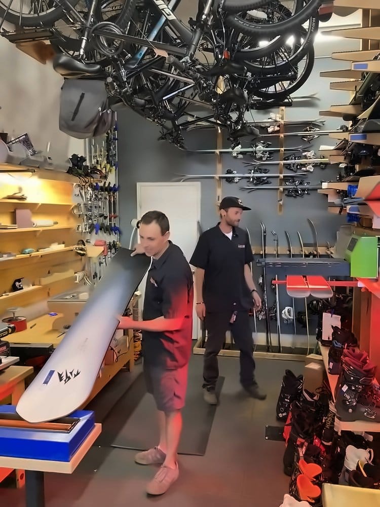 Two technicians prepping a snowboard for the wax machine
